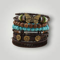 A stack of bohemian-style multi-strand bracelets on a light gray background. The bracelets feature dark brown leather, turquoise beads, wooden beads, green and white beads, and gold-toned metal accents including a butterfly charm and flower charms.
