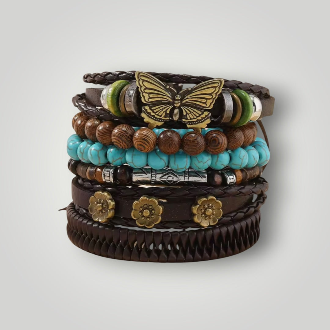 A stack of bohemian-style multi-strand bracelets on a light gray background. The bracelets feature dark brown leather, turquoise beads, wooden beads, green and white beads, and gold-toned metal accents including a butterfly charm and flower charms.