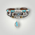 A stack of bohemian-style bracelets featuring brown leather cords, silver-toned metal beads, turquoise blue beads, and a dangling silver leaf charm with turquoise accents, displayed on a light gray background.