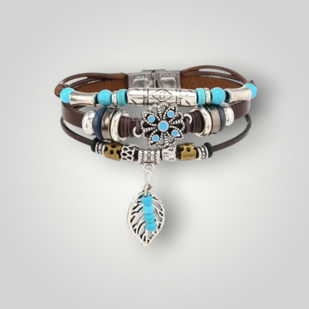 A stack of bohemian-style bracelets featuring brown leather cords, silver-toned metal beads, turquoise blue beads, and a dangling silver leaf charm with turquoise accents, displayed on a light gray background.