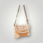 A small shoulder bag with a tan woven fabric body featuring a white hand-drawn mandala pattern on the front flap, complete with a brown leather strap and silver-tone hardware, shown against a light gray gradient background.