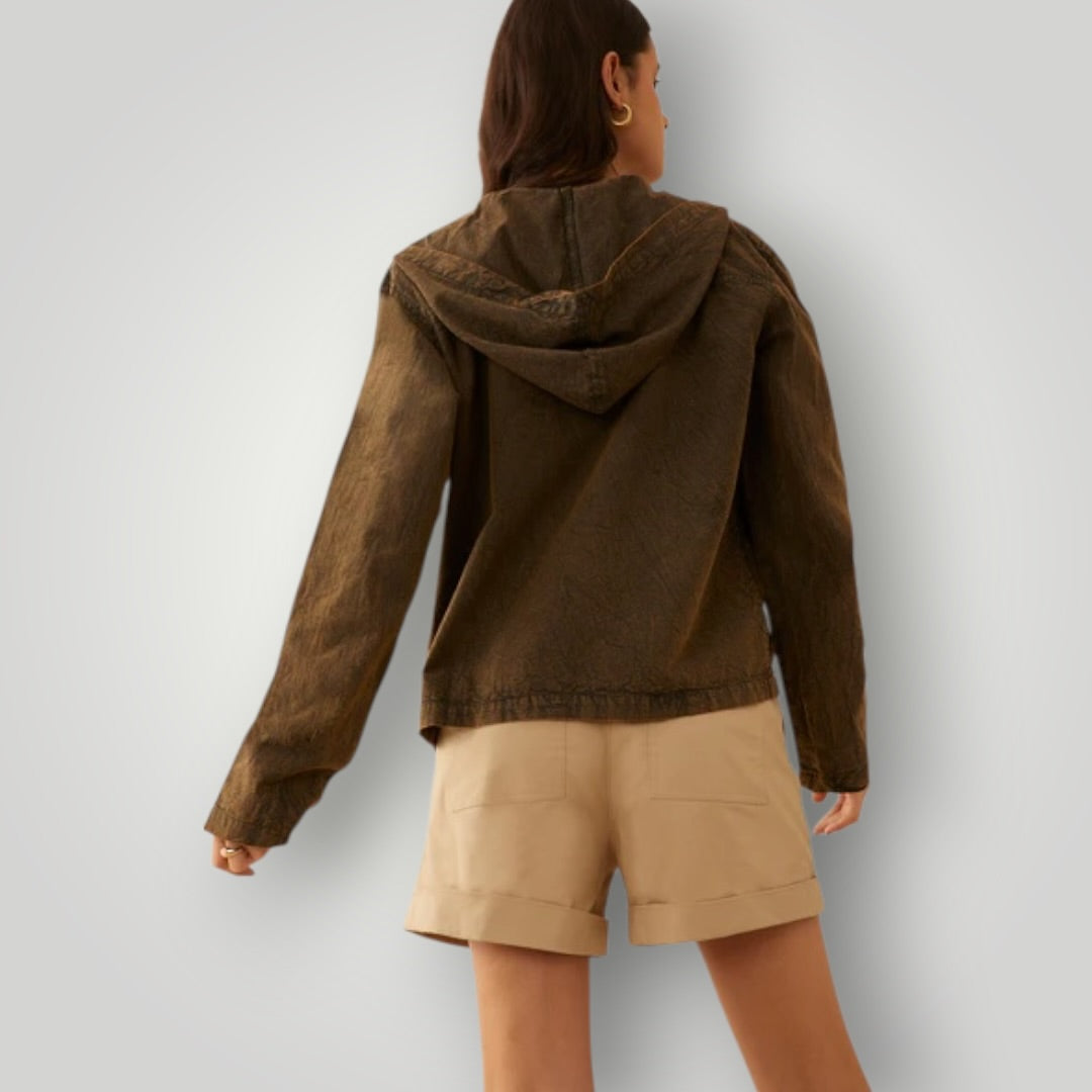 A woman shown from the back wearing a dark brown hooded jacket and beige shorts against a light gray studio background.