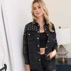 A woman modeling a black denim jacket with silver studs and silver buttons, worn over a black crop top and black denim shorts in an indoor setting.
