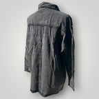A washed black denim jacket shown from the back, featuring a collar, long sleeves, and a buttoned front, photographed against a neutral light gray background.