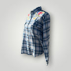 A women's long-sleeve button-up plaid shirt in shades of blue and gray, featuring colorful floral embroidery on the chest, displayed against a neutral light gray background.