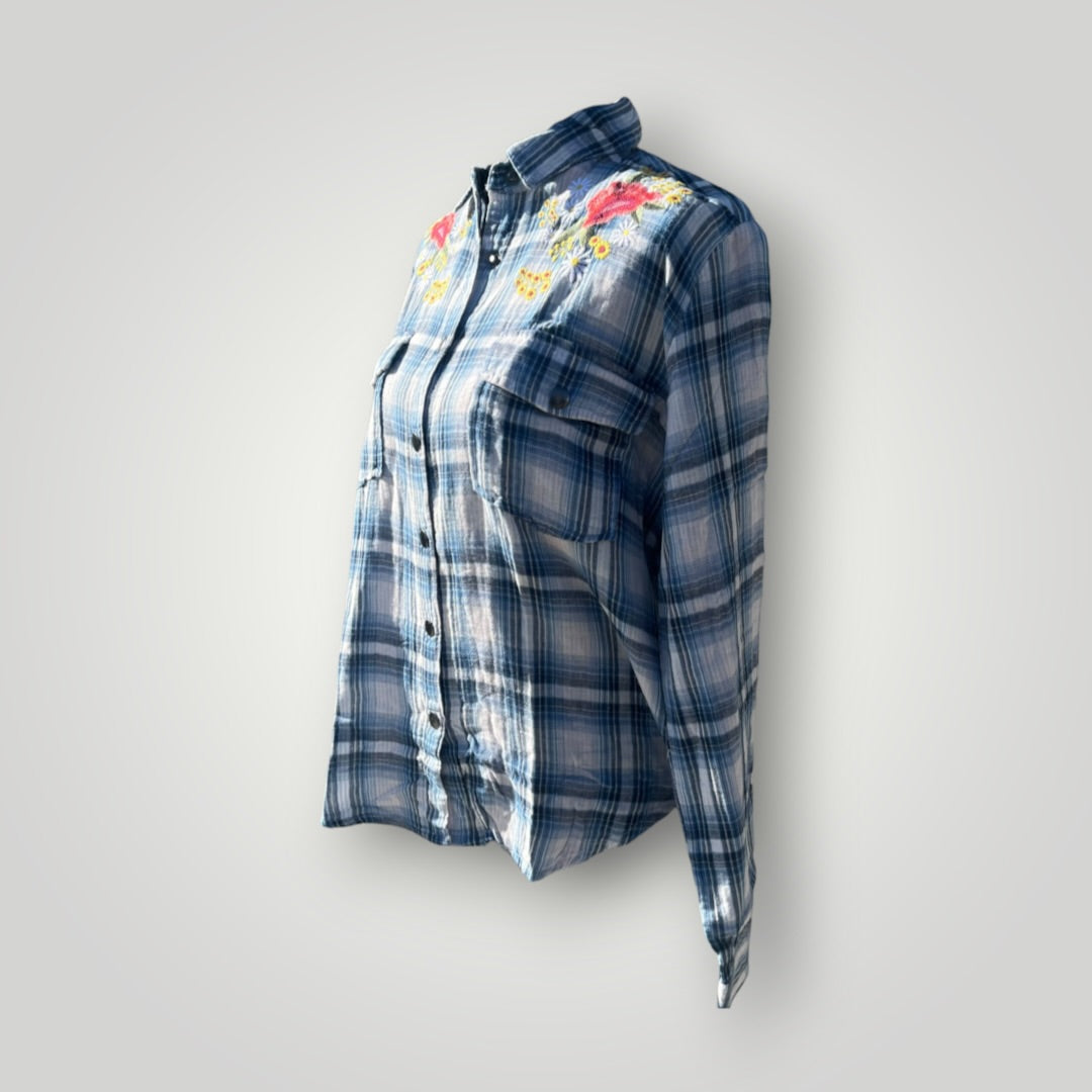 A women's long-sleeve button-up plaid shirt in shades of blue and gray, featuring colorful floral embroidery on the chest, displayed against a neutral light gray background.