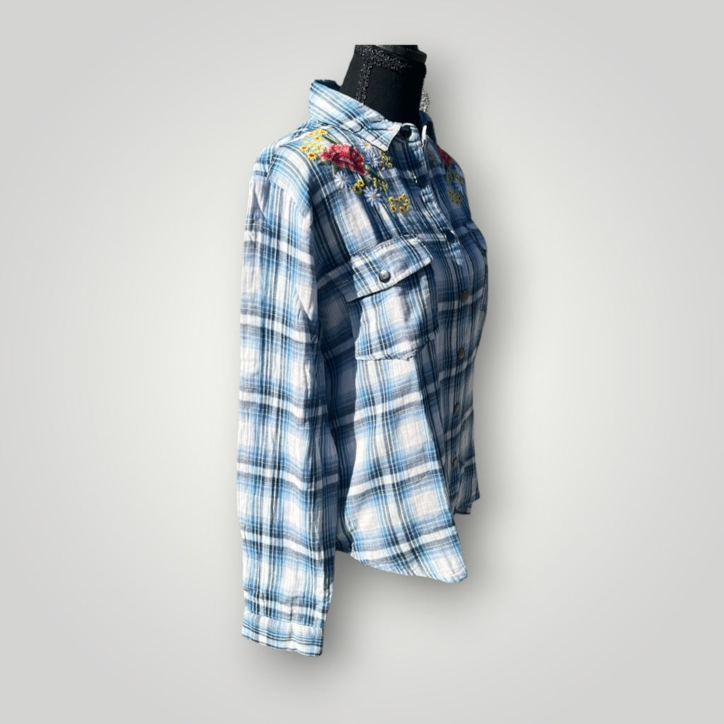 A blue and white plaid button-up shirt with colorful floral embroidery on the chest, displayed on a black mannequin torso against a light gray background.