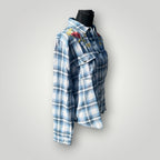 A blue and white plaid button-up shirt with colorful floral embroidery on the chest, displayed on a black mannequin torso against a light gray background.