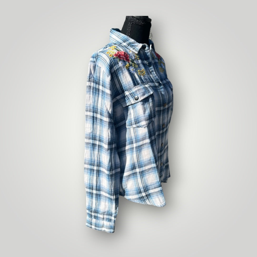 A blue and white plaid button-up shirt with colorful floral embroidery on the chest, displayed on a black mannequin torso against a light gray background.